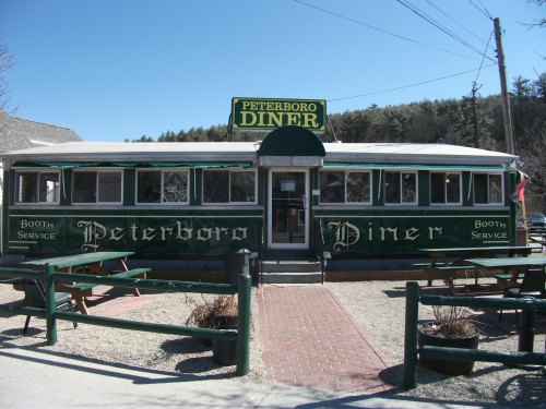 A vintage diner with green and white exterior, featuring "Peterboro Diner" signage and outdoor seating.