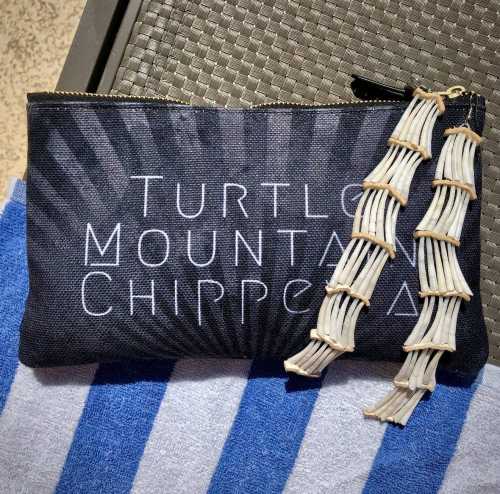 A black pouch with "Turtle Mountain Chippewa" printed on it, alongside decorative bone-like accents.