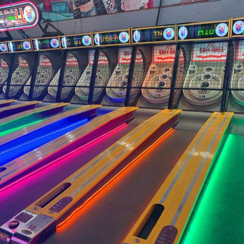 Colorful skee-ball lanes with illuminated edges and scoreboards in a vibrant arcade setting.