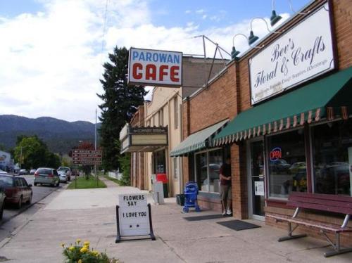A small town street featuring Parowan Café and a floral shop, with mountains in the background and a clear blue sky.