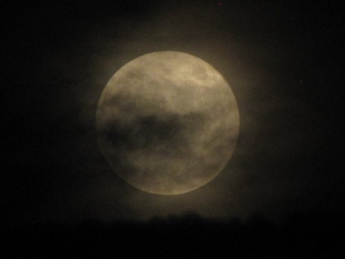 A full moon partially obscured by clouds, glowing softly against a dark night sky.
