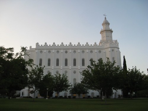 A large white building with a tall spire, surrounded by green trees and a clear sky.