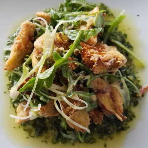 A plate of crispy fried fish pieces on a bed of green sauce, garnished with fresh greens and herbs.