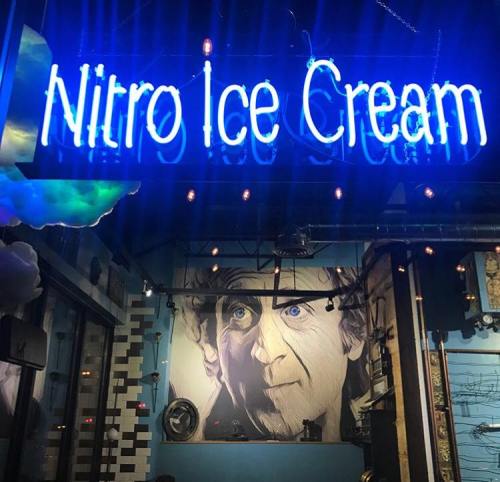 Neon sign reading "Nitro Ice Cream" above a mural of a man’s face in a colorful ice cream shop.