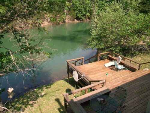 A wooden deck overlooking a calm, green river surrounded by trees and greenery.
