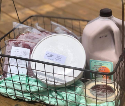 A wire basket filled with various food items, including meat packages, a gallon of chocolate milk, and a container of cream.