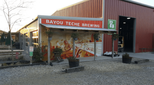 Exterior of Bayou Teche Brewing with colorful mural, outdoor seating, and a red metal building.