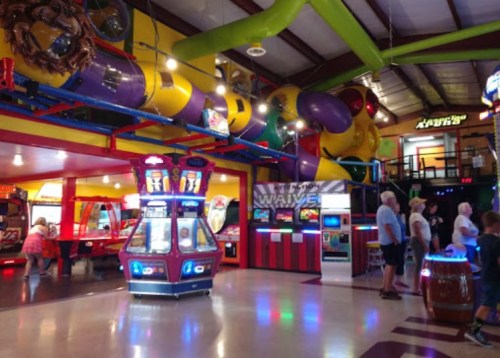 Colorful indoor arcade with games, a large slide, and people enjoying the vibrant atmosphere.