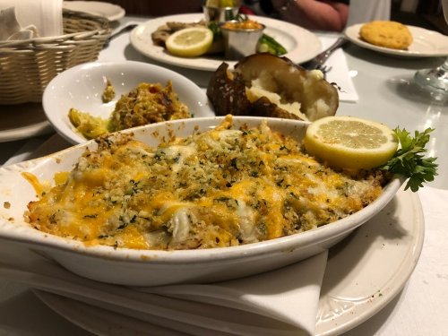 A baked seafood dish topped with cheese and herbs, served with a lemon wedge and a side of baked potato and salad.