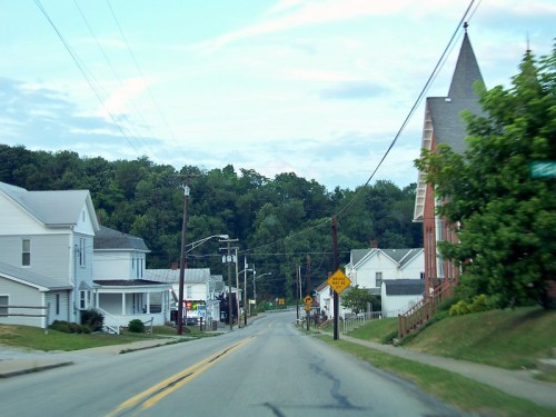 A quiet street lined with houses and trees, with a church visible on the right and a traffic sign ahead.