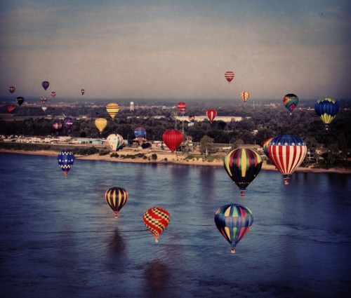 A vibrant scene of colorful hot air balloons floating over a river, with a scenic landscape in the background.