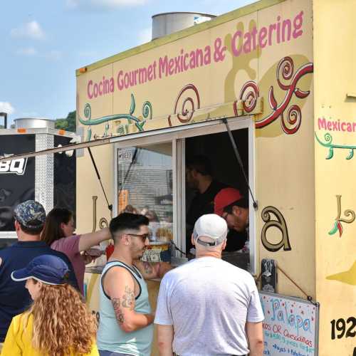 A food truck with a colorful sign serving Mexican cuisine, with customers ordering and staff preparing food.