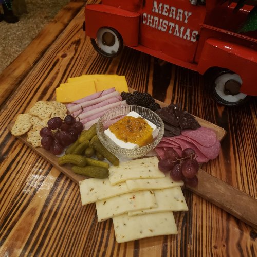 A festive charcuterie board with cheeses, meats, grapes, pickles, and a dip, set on a wooden table.