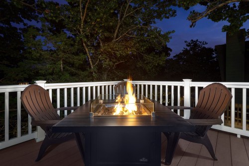 A cozy outdoor dining table with a fire pit, surrounded by trees at dusk, featuring two chairs.