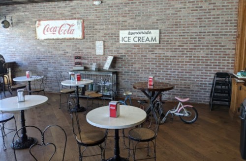 A cozy ice cream shop with wooden floors, small tables, and a vintage bicycle against a brick wall.