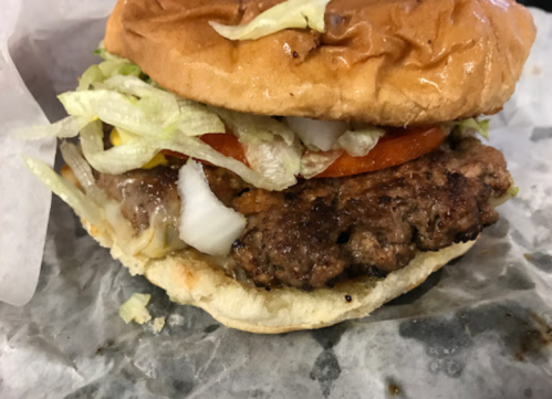 Close-up of a juicy hamburger with lettuce, tomato, onions, and mustard on a toasted bun, wrapped in paper.