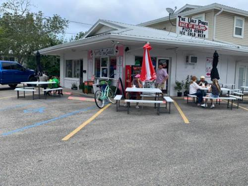 Outdoor seating area of a casual eatery with picnic tables, umbrellas, and customers enjoying food and drinks.