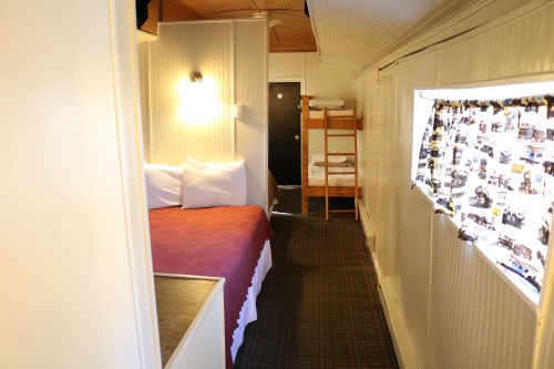 Cozy interior of a cabin featuring a double bed, bunk beds, and a window with patterned curtains.