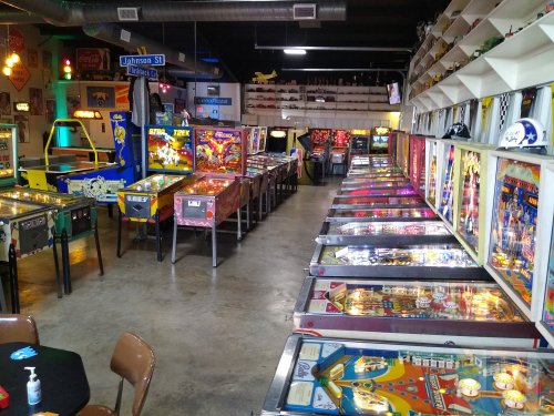 A vibrant arcade filled with various pinball machines and vintage games, showcasing colorful designs and bright lights.