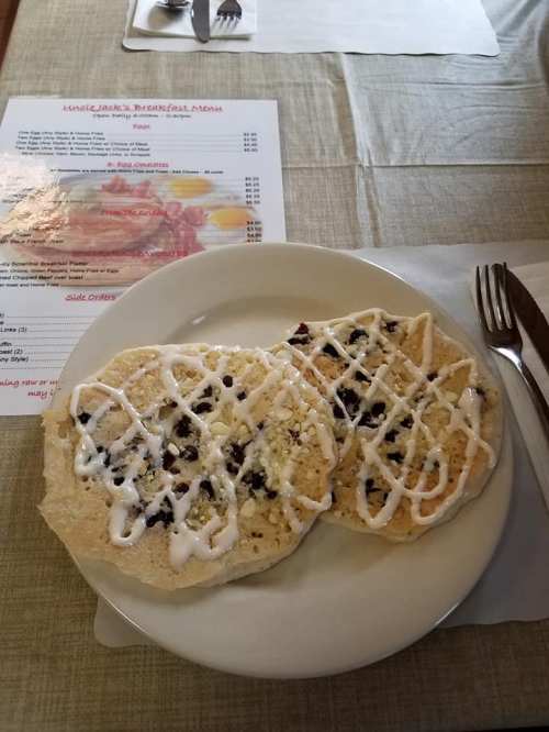 Two large pancakes drizzled with icing, served on a plate with a breakfast menu in the background.