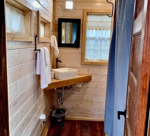 Cozy bathroom with wooden walls, a sink on a wooden shelf, towels hanging, and a mirror reflecting natural light.
