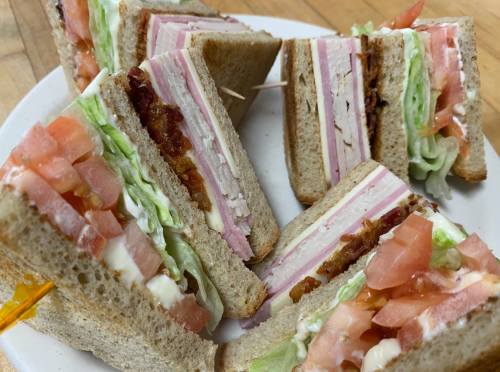A plate of stacked sandwiches with layers of ham, turkey, lettuce, tomato, and mayonnaise on whole grain bread.