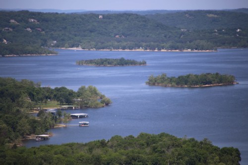 A scenic view of a lake with several small islands and lush greenery along the shoreline under a clear blue sky.