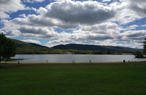 A serene lake surrounded by green hills under a partly cloudy sky.