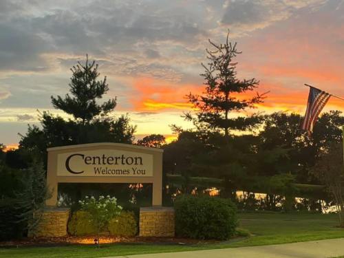 A welcome sign for Centerton at sunset, with trees and an American flag in the background.