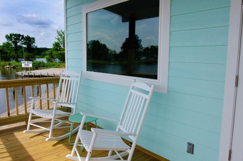 A serene porch with two white rocking chairs and a small table, overlooking a calm water view.
