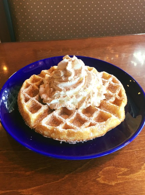 A golden waffle topped with whipped cream, served on a blue plate.