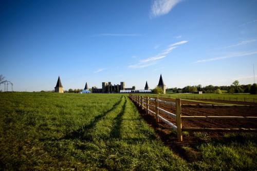 A scenic view of a green field with a wooden fence, leading to a castle-like structure under a clear blue sky.
