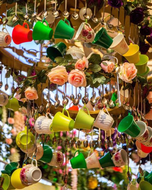 Colorful teacups and floral decorations hang from a circular structure, creating a whimsical and vibrant display.