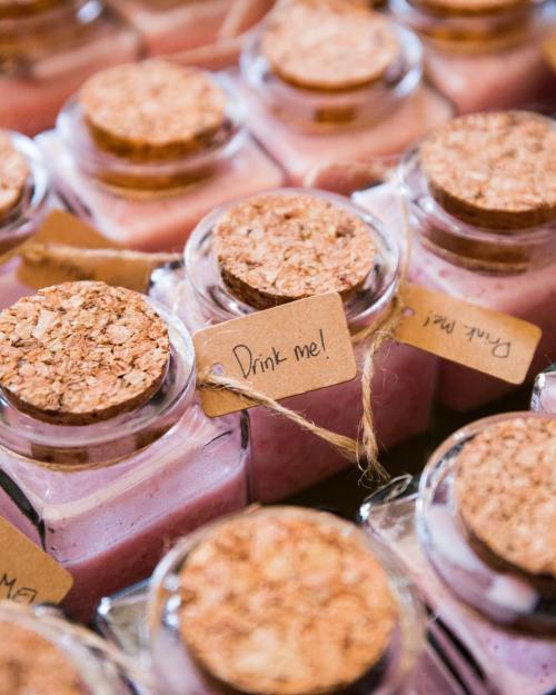 A close-up of glass bottles with cork stoppers, labeled "Drink me!" and filled with pink liquid.