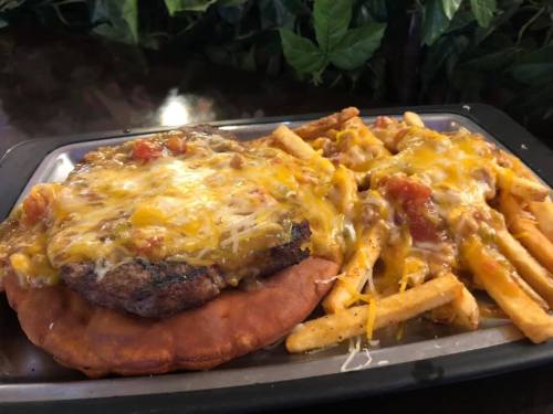 A large plate featuring a cheesy burger on a bun with fries topped in melted cheese and salsa.