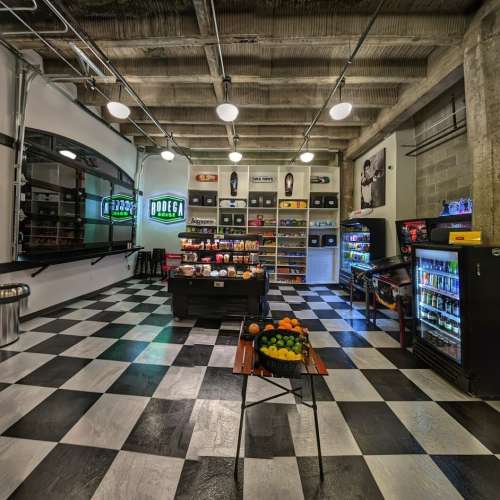A modern bodega interior with checkered floors, shelves of snacks, drinks, and a display of fresh fruits.