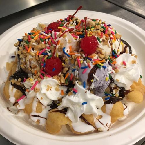 A colorful dessert with ice cream, whipped cream, sprinkles, cherries, and chocolate sauce on a plate.
