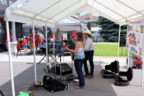 A duo performs under a tent at an outdoor event, with a crowd enjoying the music in the background.