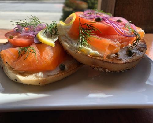 A toasted bagel topped with cream cheese, smoked salmon, capers, red onion, dill, and lemon slices.