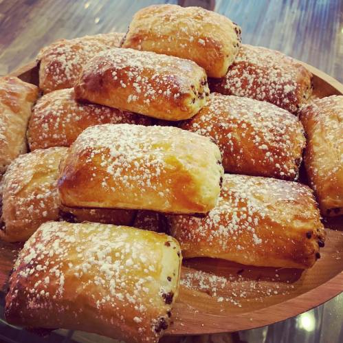 A wooden platter filled with freshly baked pastries dusted with powdered sugar.