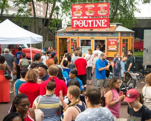 A busy food stall selling poutine, with a long line of diverse people waiting to order in an outdoor setting.