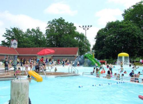 A busy outdoor pool scene with families enjoying the water, slides, and sun under a clear blue sky.