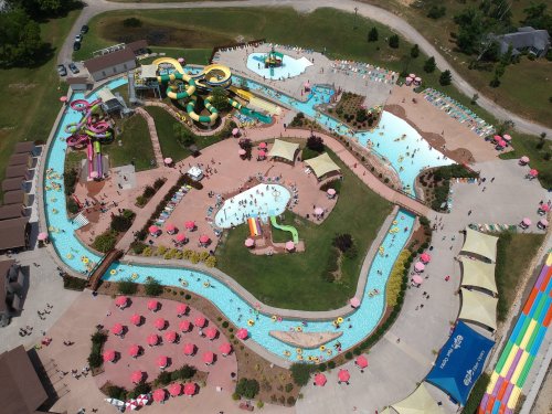 Aerial view of a vibrant water park featuring slides, pools, and lounging areas with umbrellas and visitors enjoying the sun.