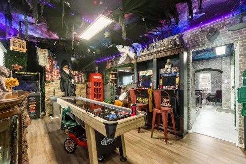 A themed game room with arcade machines, a pool table, and spooky decorations under a starry ceiling.