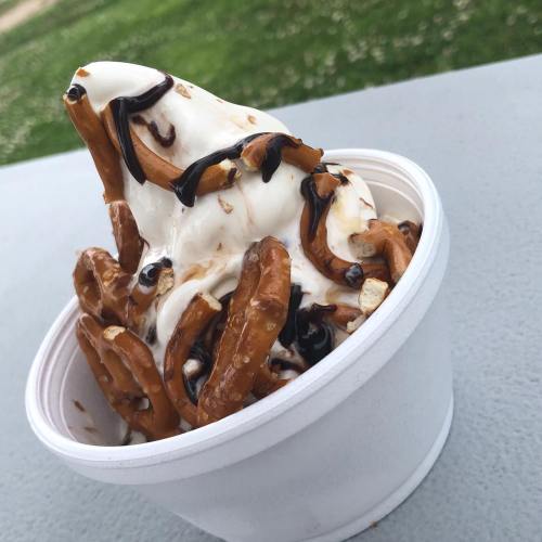 A cup of soft serve ice cream topped with pretzels and chocolate drizzle.