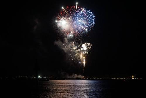 Colorful fireworks burst in the night sky over a calm body of water, reflecting vibrant lights.