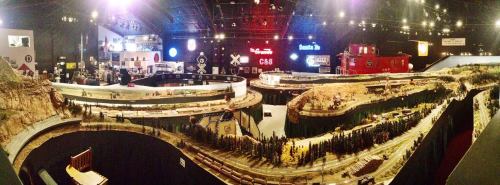 A panoramic view of a model train exhibit featuring detailed landscapes, tracks, and various themed displays.