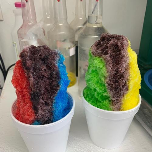 Two cups of colorful shaved ice: one with red, blue, and brown layers, the other with green and yellow layers.