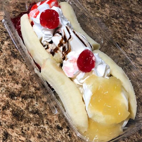 A dessert featuring three banana splits topped with whipped cream, cherries, and various fruit toppings in a clear container.