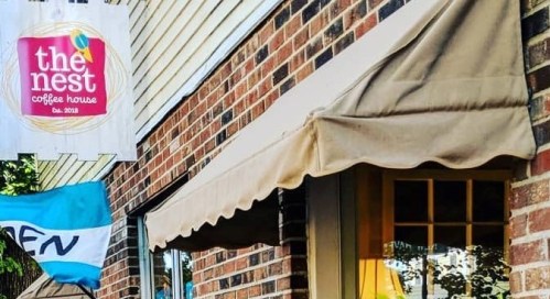 A cozy coffee house with a sign reading "the nest" and a welcoming awning, set against a brick wall.